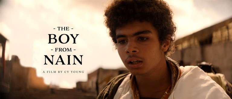 Film poster for 'The Boy from Nain,' written by Cy Young. The image shows a young boy, Benjamin, with curly hair looking intently off-camera. He is in an ancient, historical setting, with the warm, golden light of the background. The film title is prominently displayed to the left of the boy, along with the writer's name below.